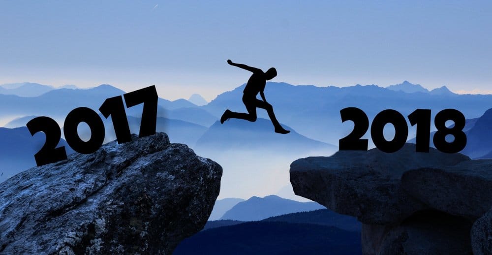 A silhouetted person leaps across a gap from one rock which says 2017, to another which says 2018. A beautiful misty mountainous landscape in the background.