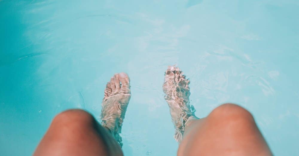 A pair of legs dangling over the clear water of a swimming pool